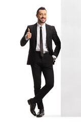 Full length portrait of a young professional man leaning on a wall and showing thumbs up