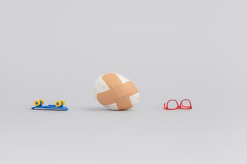 Creative food composition with broken egg with adhesive bandage and skateboard on grey background