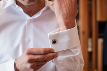 The man fastens the cufflink on the sleeve of his shirt. The groom fastens a button on the sleeve...
