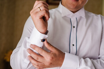 The man fastens the cufflink on the sleeve of his shirt. The groom fastens a button on the sleeve of his shirt