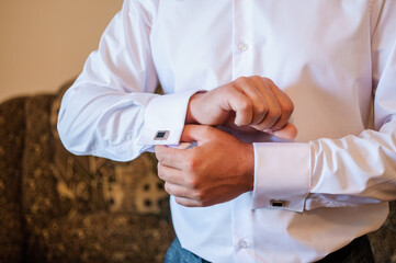 The man fastens the cufflink on the sleeve of his shirt. The groom fastens a button on the sleeve of his shirt