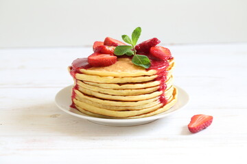 Pancakes with strawberries and mint on a white background
