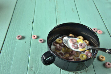 Cuchara con leche y cereales sobre un cuenco negro con cereales. Mesa de madera para copyspace 