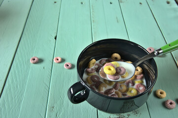 Tazón negro con leche y cereales sobre mesa de madera verde claro con copyspace.