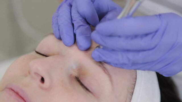 Woman beautician performs dermabrasion cosmetic procedure on client's face.
