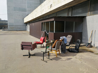 Old armchairs and chairs of various configurations and colors stand outside on a sunny day. Furniture that has fallen into disrepair is old junk.