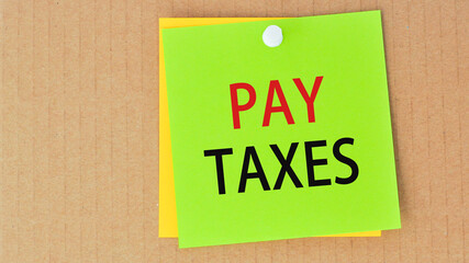 pay taxes written on green paper and pinned on corkboard,