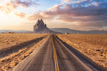 View of a road in a dry desert with a Shiprock mountain peak in the background. Sunrise Sky Art...