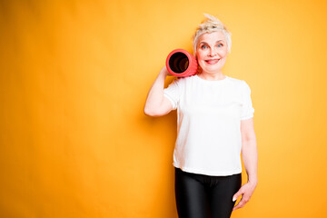 an elderly woman holds a fascia roll on her shoulder and rejoices after a fitness workout. yellow background for text