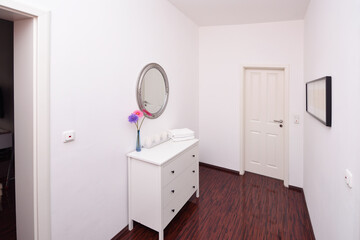 small corridor behind door with white cupboard, mirror and flowers
