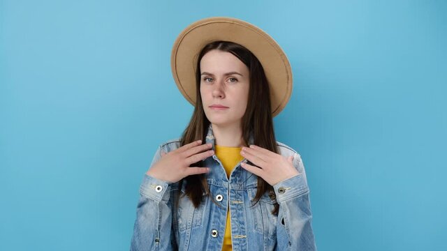 Confused young millennial woman pointing fingers herself ask say who me no thanks i do not need it, dressed in denim jacket and hat, models over blue studio background wall. People lifestyle concept
