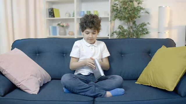 Naughty boy pretending to read, caught playing video game on couch, cheating