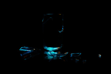 A broken drinking glass against a black background with different shards of glass reflecting at the...