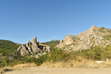 mountains and rocks covered with green plants and small houses at their base with a clear blue sky on a summer day