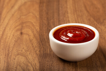 Tomato ketchup in the ramekin on wooden background.