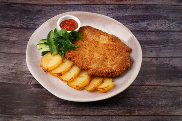 Chicken schnitzel, served with potatoes and cucumber. Natural wooden background.