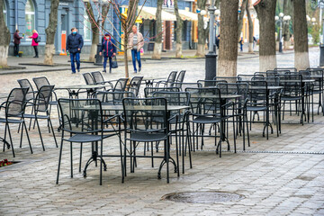 Fototapeta na wymiar Poltava, Ukraine - April 14, 2021: vintage architecture of buildings in the ancient city of Poltava in Ukraine, empty closed sidewalk cafe and walking people on the street. Lockdown in Europe 