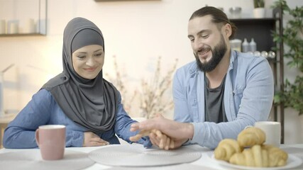 Young man holding muslim woman by hand, couple having romantic date in cafe