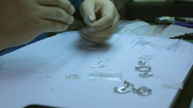 A goldsmith in jewelry checks sorting the quality of luxury brilliant diamonds . The diamonds of high caliber shine the light and pure . Many expensive and small crystals lay on table on diamond shop