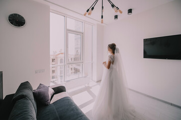 morning of the bride, getting ready, the bride in a wedding dress stands on the balcony in front of a large window