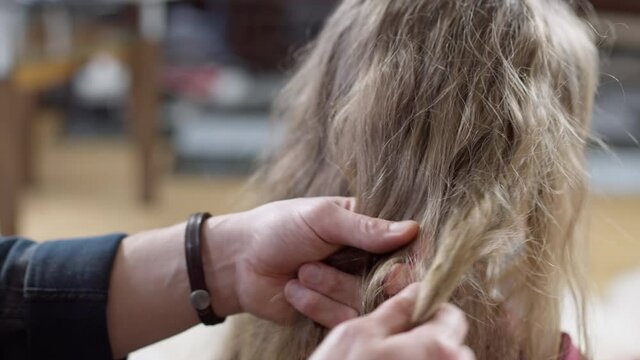 Close-up of male hands trying making pigtail on long curly child's hair. Unrecognizable Caucasian young father taking care of daughter at home indoors. Parenting concept