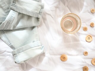 Jeans, glass and buttons on a bright white textured background.