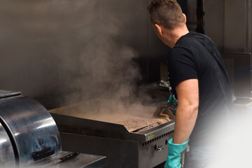 Man is cleaning grill in a restaurant kitchen