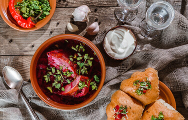 Fototapeta na wymiar Russian and ukrainian borscht or beet soup with sour cream, buns, garlic on a wooden rustic background with vodka. Top view
