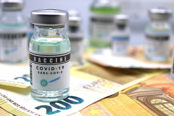 Vaccine vials next to a syringe and on euro banknotes