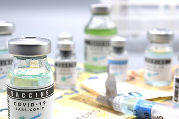 Vaccine vials next to a syringe and on euro banknotes