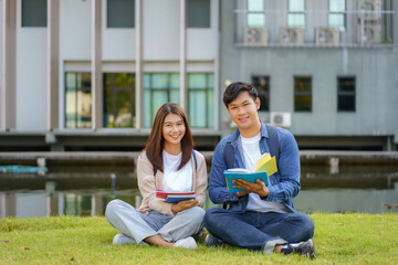 Portrait of Asian man and woman university student aitting on grass in campus looking at camera and...