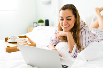 Happy woman smiling while working in bed with her laptop