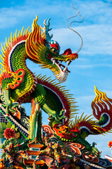Incredible statue of super colorful dragon, seated, looking back, with long ears and mustaches being illuminated by the sun, contrasting its vibrant colors with the blue of the sky.