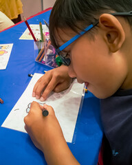 Kuala Lumpur, Malaysia - November 2019 : High angle close up of young boy tracing drawing onto a recycle plastic container sheet. Making a keychain.