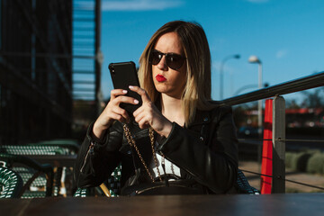 Young woman with sunglasses, typing on her mobile phone. With a street in the background. Women, smartphones and lifestyle concept. Copyspace