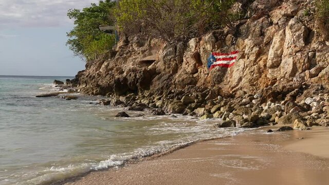 Crash Boat Beach, Puerto Rico. Painted National Flag on Rocks Above Sandy Lagoon on Sunny Day, Wide View