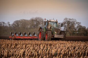 Ploughing a field at sunset with a tractor and plough, ready for crops on a farm