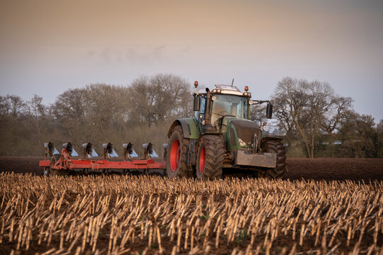 Ploughing a field at sunset with a tractor and plough, ready for crops on a farm