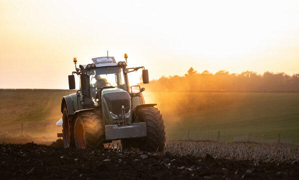 Fototapeta Ploughing a field at sunset with a tractor and plough, ready for crops on a farm