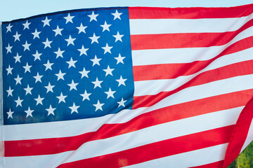 A red white and blue striped American flag hangs with trees in the background