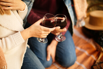 Two glasses of red wine in the hands of young people on a date. Picnic in nature, romantic trip. 