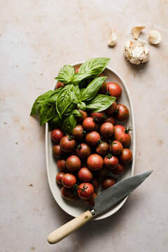 Whole and sliced cherry tomatoes in a bowl with basil and garlic cloves.