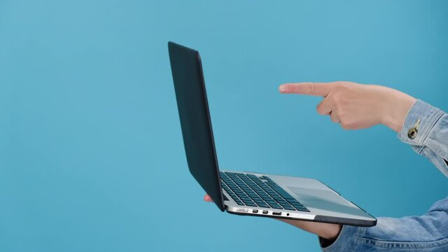 Cropped close up of female hand hold working on laptop typing on keyboard and showing thumb up as sign of approval or agreement, isolated on blue wall with copy space. Advertising workspace mock up