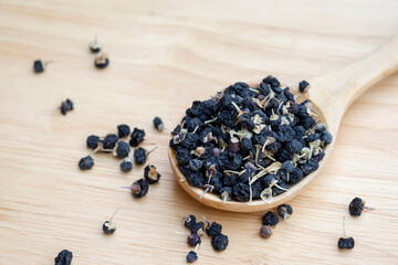 Black wolfberries or black goji berries, in a wooden spoon on table. Chinese herbs commonly used in traditional Chinese medicine. Health care concept.