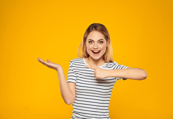 Pretty blonde on a yellow background shows her hand towards emotions positive gesture smile model