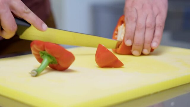 The chef cutting bell pepper using sharp knife on a chopping board.