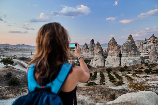 Beautiful tourist woman taking picture of Stone houses on her smartphone in Love valley in Goreme village.