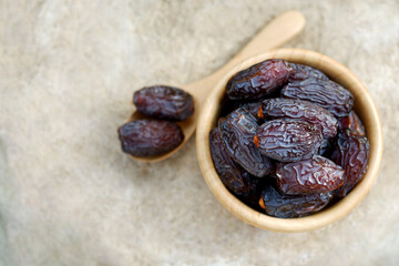 The large date palms (Medjool) in cups and wooden spoons with a cement background in top view.