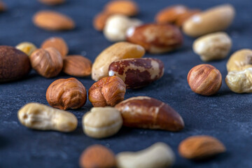 Assortment of various types of nuts on dark background. Cashew, hazelnuts, almonds and Brazil nuts close up. Healthy vegetarian snacks. Protein-containing food. Selective focus.