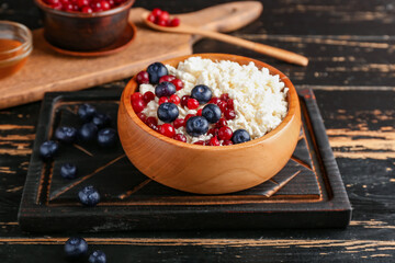 Bowl of cottage cheese with blueberries and jam on dark wooden background